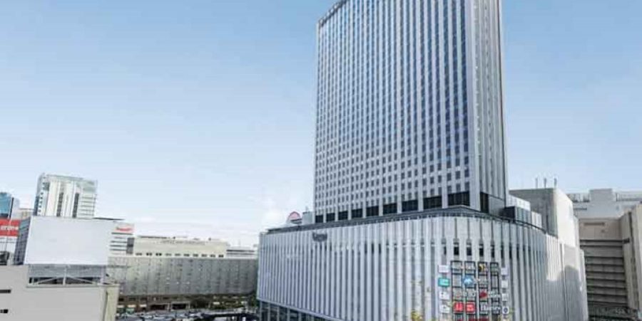 A towering building rises in the heart of a city, surrounded by urban architecture and busy streets.